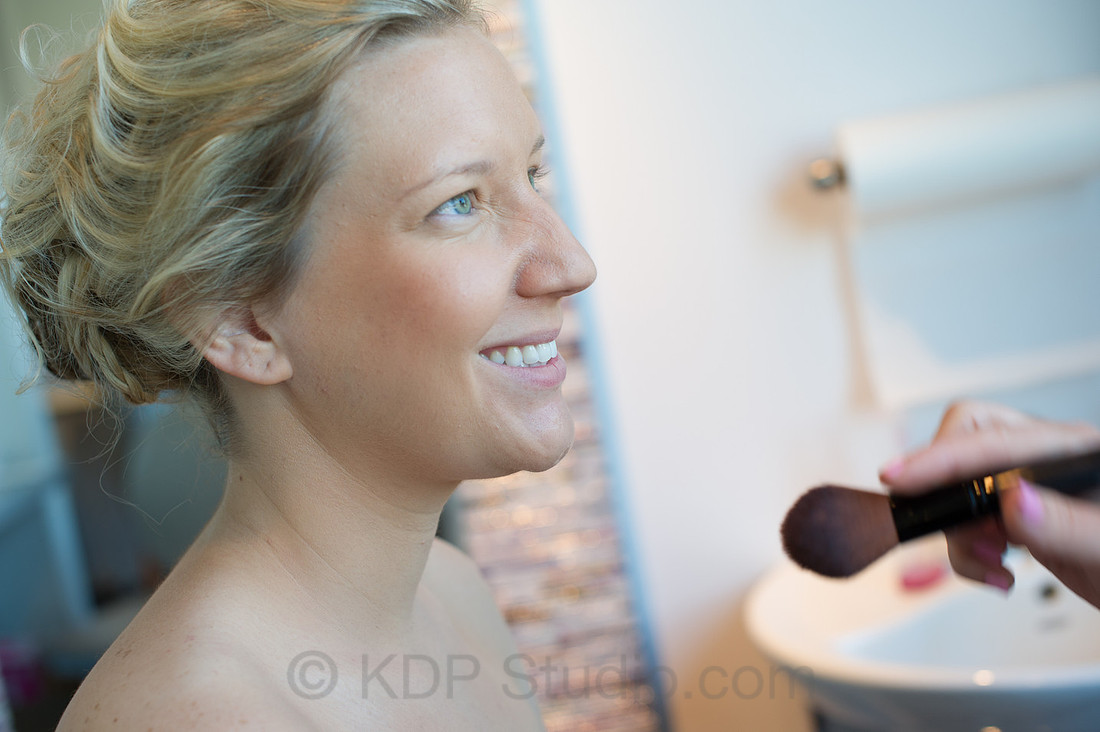 A bride smiling in profile as her makeup is finished on the morning of her wedding